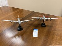 Two model airplanes on a wooden table, including Boeing B-17 Flying Fortress and B-29 models with stands and visible markings.