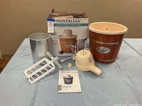 Full lot contents including Nostalgia 4-quart electric ice cream maker barrel bucket, aluminum freezing canister, white plastic paddle dasher, off-white motor housing, original product box, and instruction manual laid out on wooden floor.
