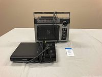 Philips DVD player DVP2800 with power cord and GE portable radio with antenna and handle shown on a light-colored surface against a plain wall.