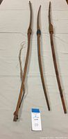 Three vintage wooden archery bows laid out on white fabric, showing their full length and curved limbs, all unstrung.