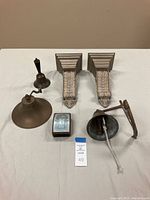 Overhead image showing three bells, Cleopatra box with mirror, and a pair of decorative wall sconces arranged on a white surface.