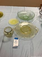 Wide shot showing all items from the lot: large serving plate with handles, small yellow plate, green uranium glass bowl and small vase.