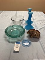 View of all lot items together: carnival glass candy dish, two frosted blue candlesticks, clear glass bowl, aquamarine ashtray and blue glass coaster.