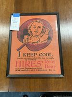 Front view of framed vintage Hires Root Beer ad with orange background showing a child holding a glass of root beer and advertisement text.