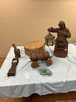 Six vintage items shown on light blue cloth: wooden circular box, miniature grandfather clock, small wooden wagon with barrel, wooden mortar and pestle, green ceramic juicer, and a metal figure holding lantern light fixture.