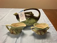Full view of vintage McCoy pottery set including teapot, creamer, and sugar bowl with green and brown pinecone and leaf pattern