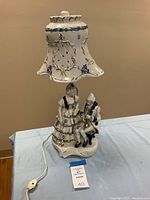 Full view of vintage porcelain lamp showing Victorian woman and man figurines and rotary switch on cord