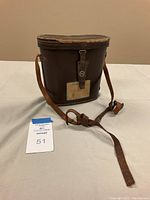 Brown leather binocular carrying case with strap, worn edges and attached buckle closure, front side view