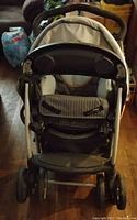Photo showing front view of beige baby stroller with padded striped seat and safety harness.