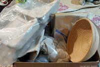 Photo showing stacked white compostable containers, round rattan proofing basket, metal trays, and cloth in packaging.