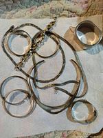 Photo showing seven silver bracelets including different styles such as open cuff, hinged bangles, and solid bands, along with three silver necklaces including a flat collar necklace and chain-link necklaces laid out on a white towel.