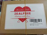 Cardboard box labeled Zealfoxe Chocolate Mold with 'Baking with Love' and a heart graphic, indicating a new chocolate heart mold inside.