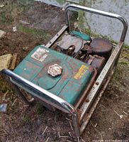 Photo of a portable gasoline-powered generator with green gas tank, metal frame showing rust and dirt, engine and other components visible.