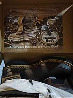 Top view of Georgia Boot branded box with image of boot on lid, showing branding and slogan 'America's Hardest Working Boot'. Open box showing one brown leather boot with rugged sole.