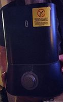 Photo of a black humidifier with a control dial and a warning label on the front.
