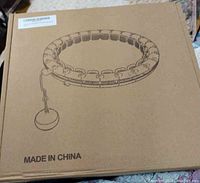 Photo of the original cardboard box containing the infinity exercise hoop, which includes an illustration of the hoop and a detachable weighted ball.
