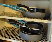 Pots and pans stacked on shelves with teal and black handles as well as various sizes of frying pans and saucepans.