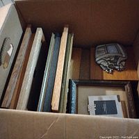 Box of assorted mostly rectangular picture frames with one ornate oval frame, showing stacked arrangement.