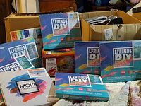 Photo showing a collection of art kits including boxes labeled 'LFRINDS DIY Digital Painting' and a brightly colored box labeled 'Aitsite One-Step Dye Kit 32 colors'. The boxes are new and unopened.