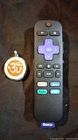 Photo shows a large, heavy pendant with silver inlay and orange Om symbol next to a Roku remote for size comparison.