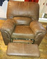 Photo of brown upholstered recliner chair with padded armrests and footrest extended on wooden flooring.