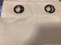 Close-up of gold-coloured fabric curtain panel showing texture and two dark brown metallic grommets