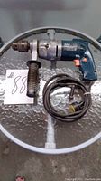 Front angle of blue and silver AEG hammer drill with side handle and coiled power cord displaying overall condition and design.