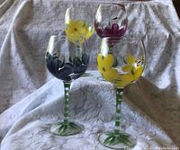 Full set of 4 hand painted wine glasses with colorful floral designs, displayed on lace fabric.
