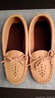 Top view of tan leather moccasin slippers showing bow detail and stitching