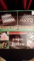 Photo showing the branding and seven different frosted glass gaming boards including chess, checkers, backgammon, poker dice, dominoes, cribbage, and cards with the 'Lucky 7 Gaming Classics' label.