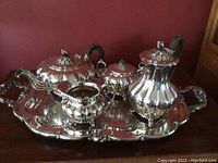 Overall view of the full tea and coffee service set with tray on a surface against a burgundy wall.
