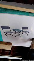 Photo of packaged 3-piece steel bistro set with image of product showing table and two chairs.