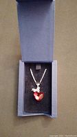 Front view of the red Swarovski crystal heart pendant with silver chain inside original blue Swarovski box.