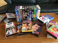 Photo showing a variety of VHS tapes arranged on a coffee table with visible titles including 'Roman Holiday', 'Harry Potter', 'Big', and others, illustrating the condition and breadth of the collection.