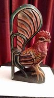 Photo of colorful carved wooden rooster, showing detailed paint and carving on feathers, standing upright.