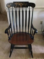 Front view of Hitchcock rocking chair showing black frame, brown contoured seat, spindled back and armrests