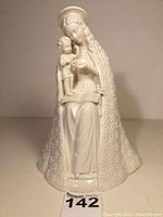 Front view of white porcelain Flower Madonna figurine showing Mary seated holding baby Jesus standing on an open book, cloak decorated with embossed flower pattern