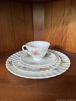 Stacked set of plates and a teacup showing the scalloped edges and floral designs.
