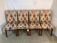 Four dining chairs with multicolored patterned upholstery and wooden legs, displayed against a white background.