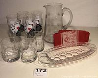 Full lot: star pattern cut glass pitcher, sets of drinking glasses, diamond cut dish, and tea towel arranged on table.