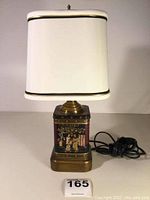 Full view of lamp showing white cloth shade and chinoiserie tea tin base with brass components and power cord