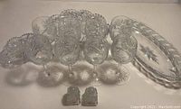 Thirteen vintage crystal pieces arranged on a white surface including 3 oval bowls of different sizes, 8 wine glasses, and 2 salt and pepper shakers, all with starburst and cut glass patterns.