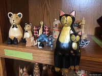 Photo showing an assortment of wooden animal figurines including two large black and yellow cats, bears, owl, mice, turtle, and other small animal figurines.