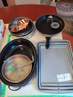 Copper mold, bundt cake pan, springform pans, pie pans, toaster with lid, timer and mesh strainer on table with a rug in background