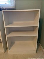 Front view of the white MDF bookcase showing three shelves and side peg holes for adjustable shelves.