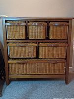Front view of wood-framed cabinet showing six woven wicker basket drawers arranged in two columns on three shelves.