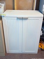 Front view of white plastic storage cabinet closed with 2 doors, showing vertical ribbed design and horizontal door handles.