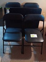 Front view of four black vinyl upholstered folding chairs with metal frames, arranged in two rows.