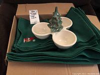 Stack of 10 green placemats with embroidered snowman and napkins with three-section ceramic dish topped with Christmas tree decoration