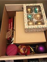 Photo of a large box with various loose ornaments and original boxes inside, some glass and some fabric ornaments visible